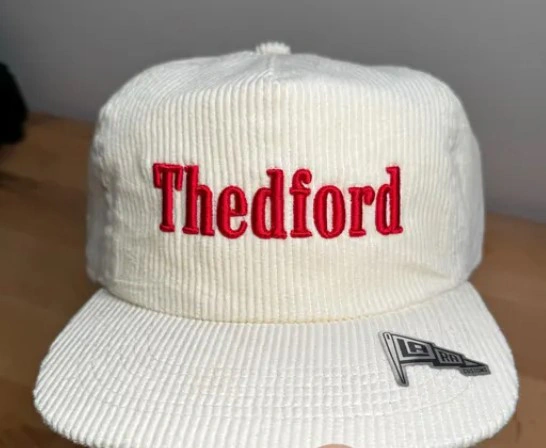 White ribbed cap featuring red Thedford lettering embroidered across the front panel.